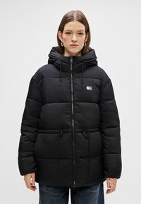 Mustat puffatakki huppuineen, jossa on vetoketjukiinnitys, säädettävät nyörit ja pieni logopatch. Pehmeä, tikattu materiaali.