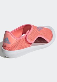 Sneaker in rete rosa con suola bianca, dotata di una fascetta in velcro e di un colletto imbottito per il comfort. Logo adidas visibile sul lato.