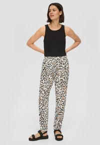 Czarny top na ramiączkach zestawiony z lekkimi, kremowymi spodniami w leopardzie plamki z pomarańczowymi i niebieskimi kropkami, uzupełniony czarnymi sandałami.
