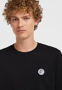 Sort bomulds-sweatshirt med rund halsudskæring, udstyret med et cirkulært logo-patch på venstre bryst. Glat tekstur og standard pasform.