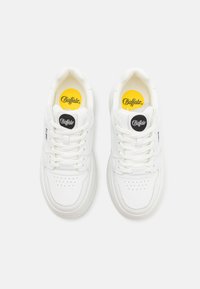 Baskets blanches avec une tige en cuir lisse, bout rond, détails perforés et lacets plats. Présente des logos noirs et jaunes sur la languette.