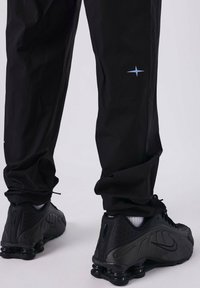 Pantalones deportivos negros y zapatillas Nike negras con un acabado texturizado, que presentan una estrella de acento azul claro en la pierna izquierda.