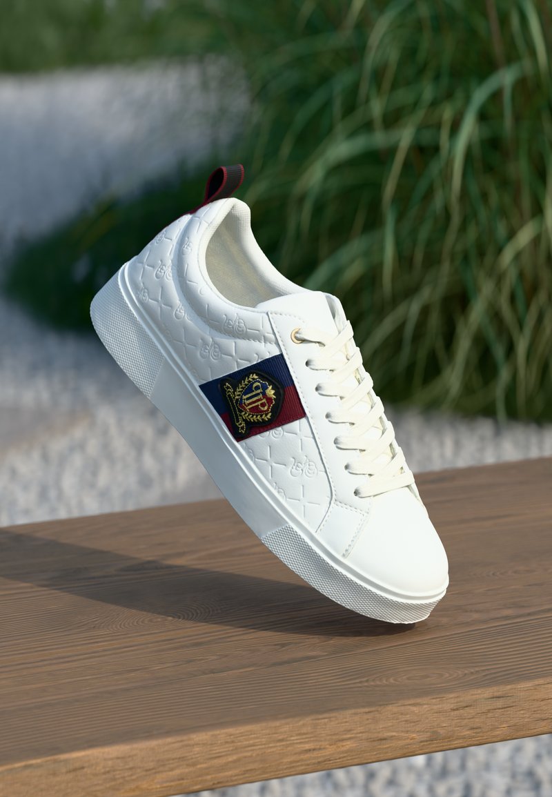 Baskets en cuir blanc avec une surface texturée, panneau latéral rouge et marine, œillets dorés et semelle en caoutchouc blanc, exposées sur une surface en bois.