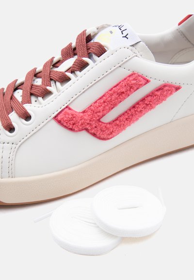 Λευκό δερμάτινο αθλητικό παπούτσι με ροζ ανάγλυφο λογότυπο και καφέ κορδόνια, συνοδευόμενο από δύο κουλουριασμένα λευκά εφεδρικά κορδόνια σε λευκό φόντο.