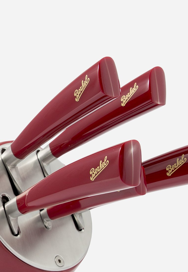 Rote Messergriffe mit glänzender Oberfläche und goldenen Akzenten, in einem Halter aus Edelstahl. Das Design zeigt drei gebogene Griffe.