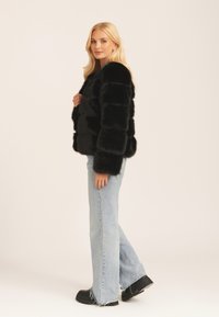 Black faux fur cropped jacket with horizontal stripe texture, paired with light blue flared jeans and black platform boots.