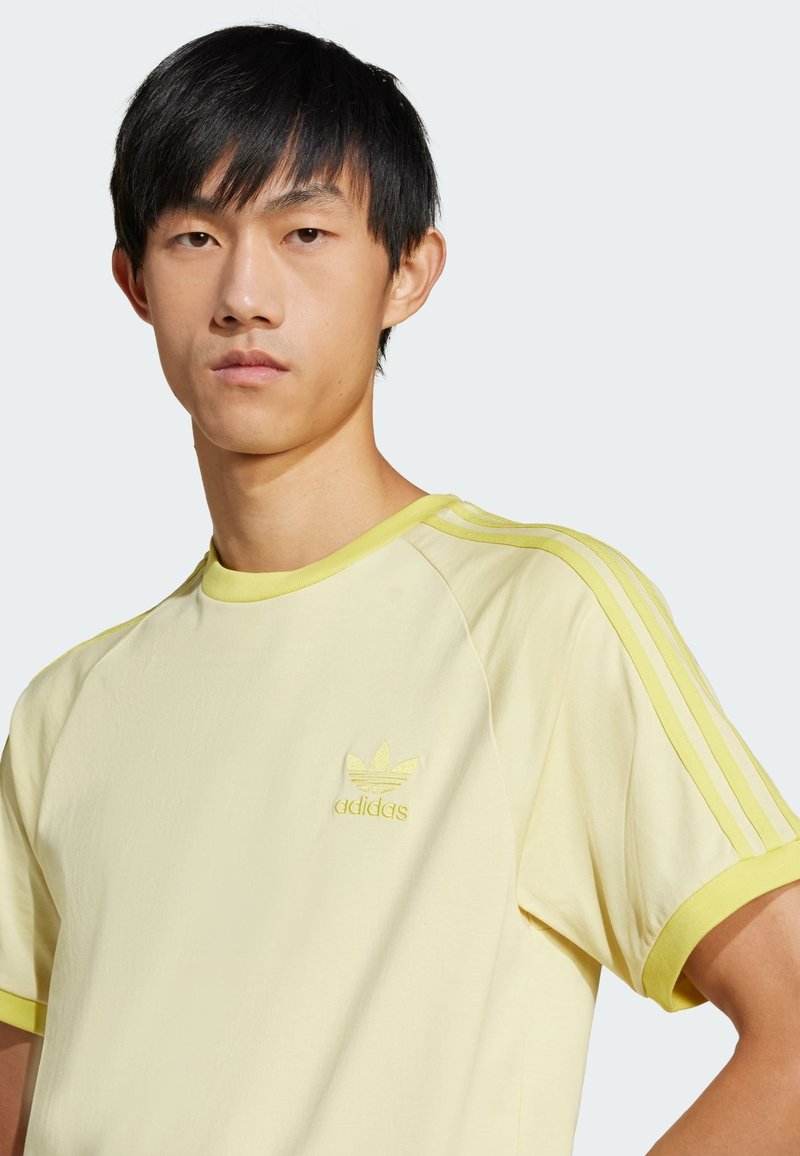 T-shirt gialla con tre strisce orizzontali sulle maniche, logo ricamato sul petto, realizzata in tessuto morbido, con scollo rotondo.