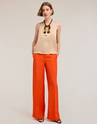 Top sin mangas beige con escote redondo, combinado con pantalones anchos de color naranja brillante. El look incluye un collar decorativo con borlas.
