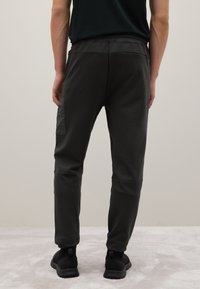 Dunkelgraue Jogginghosen aus einem glatten Stoff, mit einem elastischen Bund, schmal zulaufenden Hosenbeinen und einer seitlichen Tasche mit einer strukturierten Applikation.