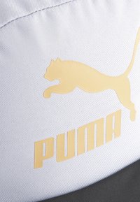 Puma kapa s karakterističnom teksturiranom svijetlosivom tkaninom, istaknutim zlatnim logotipom skakačkog tigra i podebljanim slovima "PUMA" u zlatnoj boji.