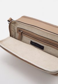 Kremowy, syntetyczny skórzany portfel typu kopertówka z zamkiem błyskawicznym, z beżową lnianą podszewką, jedną zasuwaną kieszonką i wszytą metką.