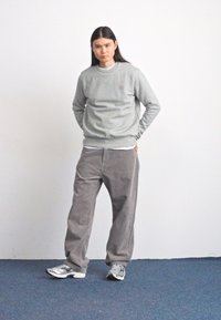 Grå sweatshirt over en hvid skjorte, parret med løse, grå fløjl bukser. Outfittet har et logo på brystet og grå sneakers.
