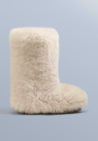 Crèmekleurige laars van imitatiebont met een zachte, pluizige textuur, een afgeronde neus en een dikke zool, ontworpen voor comfort en warmte.