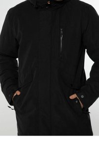 Mustat takki, jossa on vetoketjullinen rintatasku, nappikiinnityksellä varustetut sivutaskut ja säädettävä nyöri-huppu. Valmistettu teksturoidusta kankaasta.