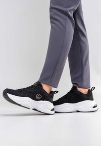 Schwarze Sportsneaker mit strukturiertem Obermaterial, weißer Zwischensohle und schwarzem Gummi-Außensohle, ausgestattet mit einem Logodetail an der Seite und Schnürsenkeln.
