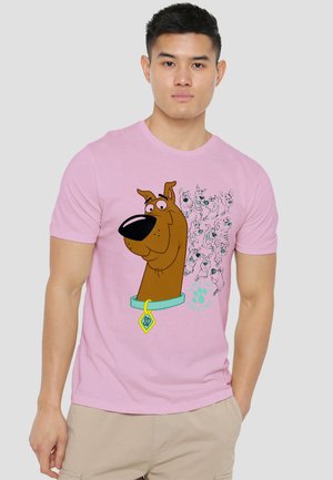 Man wearing a pink t-shirt featuring a large cartoon dog head with a blue collar and small dog sketches on a light background.