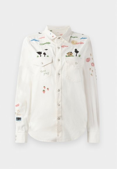 Valge nööpidega särk, millel on tikitud värvikad pilved, puud, maja, maasikad, kõrvitsad ja fraas "puuduta rohtu" esiküljel.