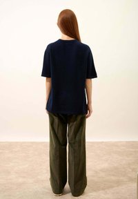 Granatowa bluzka z krótkim rękawem z teksturowanej tkaniny, zestawiona z luźnymi oliwkowymi spodniami. Prosty fason o swobodnym kroju.