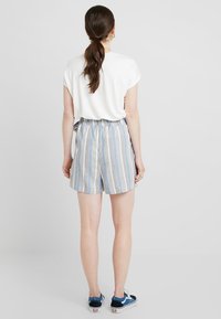 Randiga blåa och vita shorts i lätt tyg, med elastisk midja, tillsammans med en kortärmad vit topp och avslappnade sneakers.