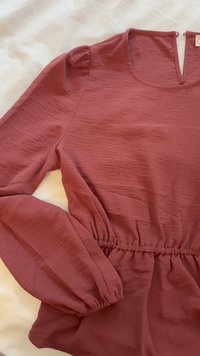 Maroon blouse with a textured surface, scoop neckline, and elasticized waist. Features puffed sleeves and a pleated design detail.