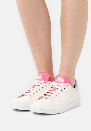 Białe skórzane sneakersy z różowymi i miętowymi akcentami, z perforowanymi detalami i białymi gumowymi podeszwami. Sznurowadła są różowe.