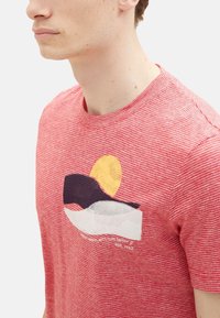 Rot-weiß gestreiftes T-Shirt mit Rundhalsausschnitt, das ein grafisches Design einer gelben Sonne und abstrakten Formen in Blau und Weiß zeigt.