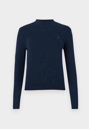 Navy blue long-sleeve turtleneck top, ribbed texture, featuring a small logo on the chest, with a fitted design and crew neckline.