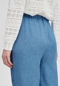 Pantaloni di lino blu con una vestibilità rilassata e cintura elastica, abbinati a un top bianco lavorato a maglia con un motivo a diamante.