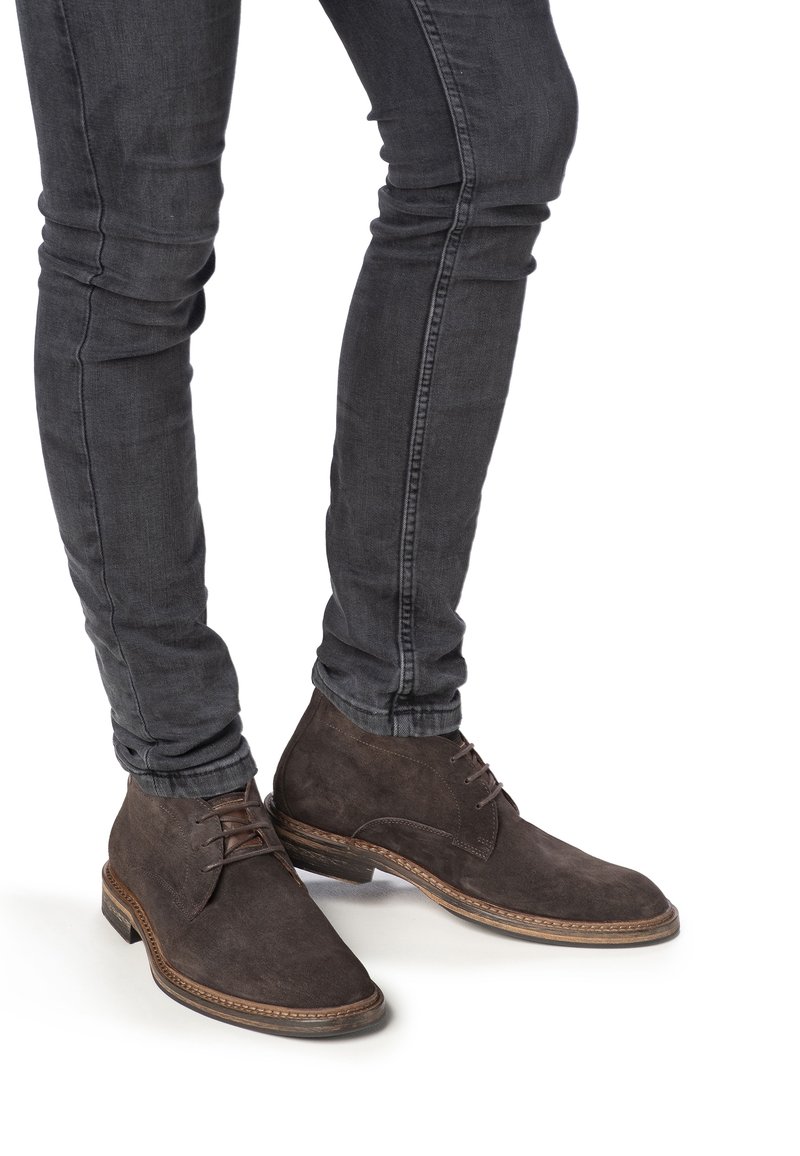 Bottes de chelsea en daim gris foncé avec lacets, présentant un bout rond et une surface texturée, associées à un jean slim foncé.