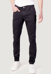 Pantalones cargo negros de mezcla de algodón, con múltiples bolsillos, ajuste slim y cierre frontal con botones. Combinados con zapatillas blancas.