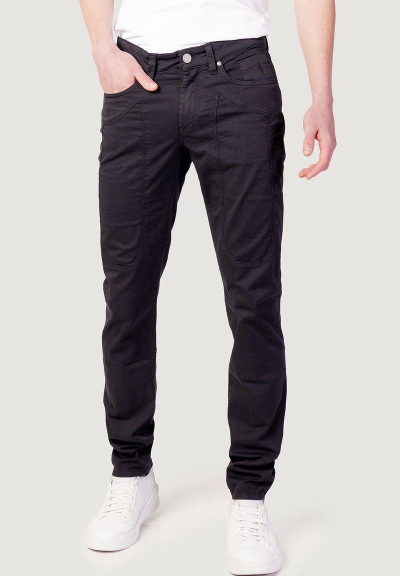 Pantalones cargo negros de mezcla de algodón, con múltiples bolsillos, ajuste slim y cierre frontal con botones. Combinados con zapatillas blancas.