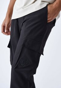 Pantalones cargo negros hechos de una tela resistente, con bolsillos laterales, un detalle de logo bordado y un corte relajado con una textura suave.
