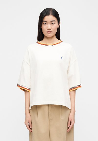 Biele tričko s krátkym rukávom a guľatým výstrihom, zdobené oranžovým a červeným prešívaním pozdĺž výstrihu a rukávov, s malým logom na hrudi.