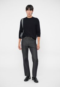 Czarny sweter dzianinowy zestawiony z ciemnoniebieskimi spodniami dżinsowymi. Model nosi czarne buty i szary torbę na ramię. Czysty, minimalistyczny styl.