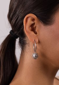 Silberne Creolen mit einem Sonnenstrahlen-Design, das eine zentrale Kugel umfasst. Die Ohrringe hängen unterhalb des Ohrläppchens und zeigen aufwendige Details.
