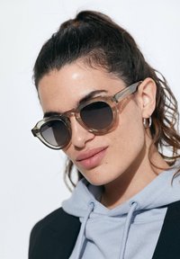 Ümmargused, läbipaistvad prillid tumedate läätsedega; heledast pruunist kilpkonnakilbist raami; selged käeaktsendid; kantud helesinise kapuutsiga ja musta ülikonna kombinatsiooniga.