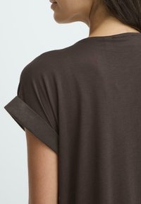 Mørkebrune kortærmede top med en afslappet pasform. Blødt, glat stof; rullede manchette detaljer. Simpelt design uden synlige mønstre eller accenter.