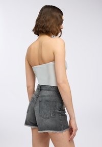 Jasnoszary top bez ramiączek o gładkiej fakturze w połączeniu z czarnymi, wysokozamykanymi szortami dżinsowymi z przetarciami, z postrzępionymi końcami i tylnymi kieszeniami.