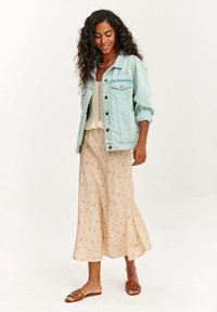 Jasnoniebieska dżinsowa kurtka, kremowy top z koronkowych splotów, swobodna beżowa spódnica w kwiatowe wzory oraz brązowe płaskie sandały. Miękkie tkaniny i luźny krój.