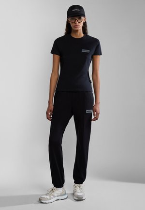 Black fitted t-shirt with logo, matching black joggers, and a black cap. Model wears clear sunglasses and light colored athletic shoes.