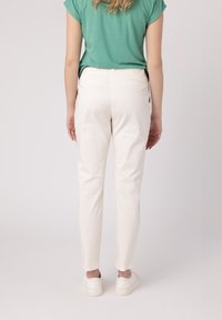 Biele slim-fit nohavice s hladkou textúrou, zúženými nohavicami a bočnými vreckami, spárované so zeleným topom s krátkym rukávom a bielymi teniskami.