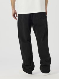 Crne traper hlače širokog kroja, s dva stražnja džepa i suptilnim detaljima šavova, uparene s bijelim tenisicama.