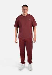Bordeaux katoenen t-shirt en bijpassende joggingbroek met elastische boorden, gecombineerd met witte sneakers. Eenvoudig ontwerp met minimale details.
