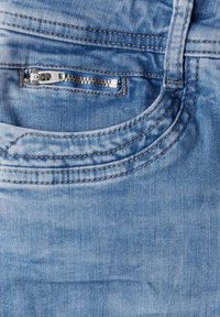 Vaqueros de mezclilla azul claro con un cierre metálico visible y un bolsillo delantero. Presenta costuras en contraste y un acabado suave y texturizado.