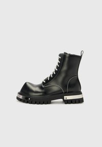 Melnas ādas potīšu zābaki ar masīvu zoli, kontrastējošām baltām šņorēm un sudraba detaļām. Gluda virsma ar noapaļotu purngalu.