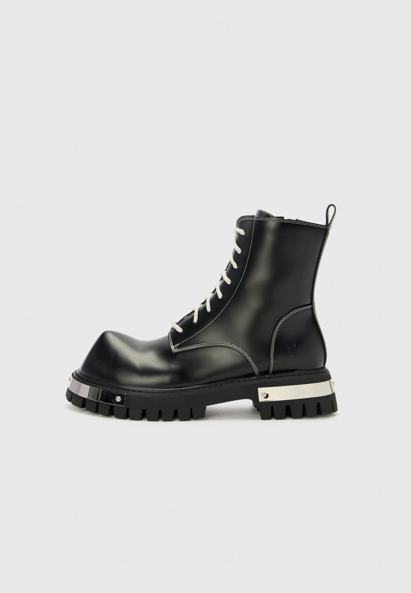 Botine negre din piele, cu o talpă groasă, șireturi albe contrastante și accente din metal argintiu. Textură netedă cu un design cu vârful rotund.