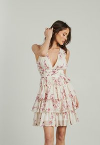 Sukienka w kształcie litery A z drukowanym wzorem kwiatowym, z głębokim dekoltem w kształcie litery V, regulowanymi ramiączkami, warstwowymi falbanami oraz lekkim, teksturowanym materiałem w odcieniach kremu i różu.