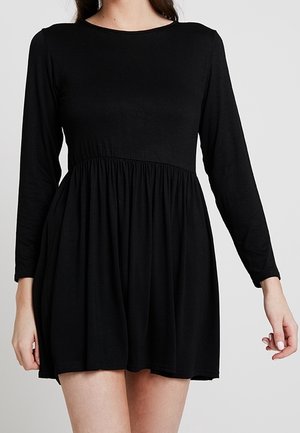 Robe noire en tissu doux et léger. Elle présente des manches longues, un décolleté arrondi et une taille froncée qui s'évasent en jupe.