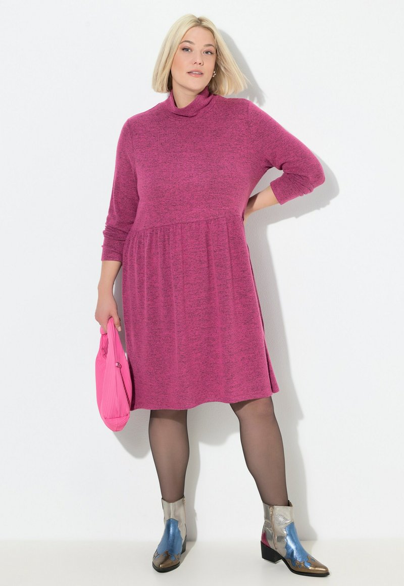 Langärmelig, coltrui-jurk in gestructureerd magenta, getailleerd, gecombineerd met multikleurige metallic enkellaarzen en een roze tas.