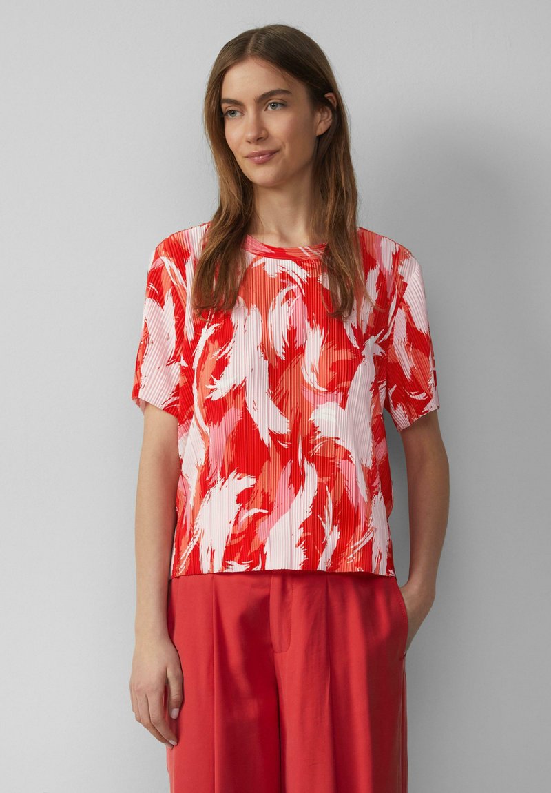 Rood en wit kortegemouwenshirt met een bloemenpatroon en geplooide textuur, gecombineerd met koraalkleurige wijde broek.